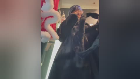 Video of a person in a dark coat, holding a black dog, with a large, plush, white and red rabbit in the background.