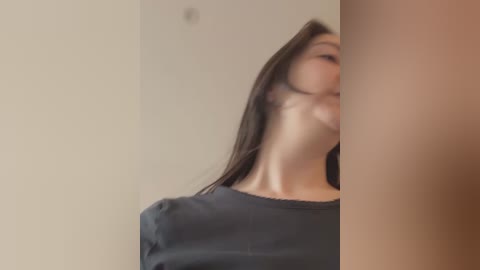 A video showing a close-up of a woman with long, dark hair, wearing a dark shirt, standing against a beige wall. The image is slightly blurred.