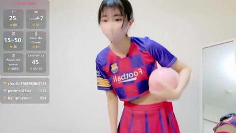 Video of a young East Asian woman in a Barcelona soccer jersey, mid-action, holding a pink ball in a mirror-clad room.