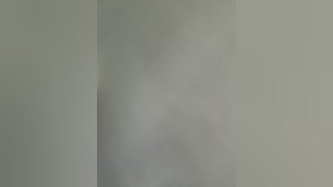 A blurred video of a white wall with a faint shadow suggesting a person or object standing in front of it, creating a subtle contrast. The image is minimalistic and lacks specific details.