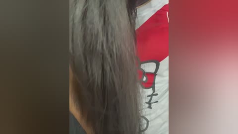 A close-up video of a person with long, straight, dark hair, partially obscured by a red and white graphic t-shirt. The background is blurred and indistinct.