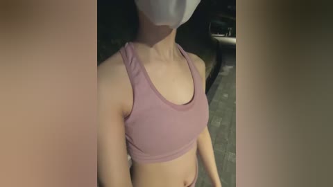 Media: A video of a light-skinned woman wearing a white face mask and a pink sports bra, taken indoors with blurred background.