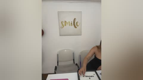 Video of a dental office with a white chair and a woman in a black sleeveless top, working on a patient's teeth. The wall features a framed, modern artwork with the word \"smile\" in gold and black letters.