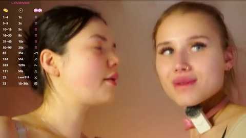 Video of two young Asian women with fair skin, one with dark hair in a ponytail, the other with blonde hair in a ponytail, smiling and applying makeup.