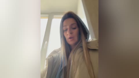 Media: A video of a young woman with long, straight brown hair, wearing a beige coat, sitting in a car with light streaming through the window.