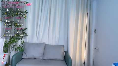 Video of a modern living room with a white sofa, green armchair, and a tall floor lamp beside a white curtain. The image has a virtual camera overlay showing room dimensions and measurements.