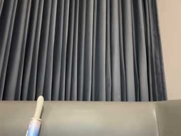 Video of a dark gray pleated curtain with vertical folds, covering a white wall. A white toothbrush is partially visible at the bottom left corner.