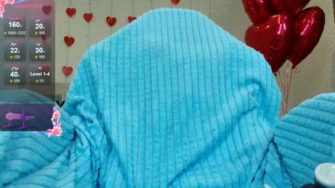 Video of a cozy, blue, textured blanket draped over a bed, with red heart-shaped balloons and a digital clock showing 15:06 on the left.