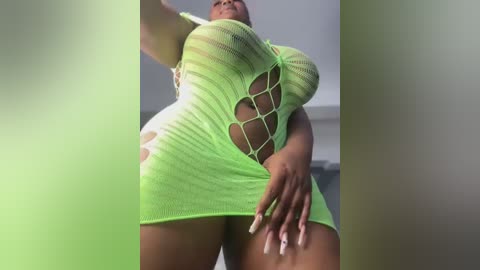 Video of a curvy, dark-skinned woman wearing a neon green, sheer, lace dress with large cutouts, revealing ample cleavage and bare thighs. The background is blurred.