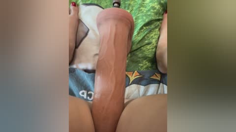 Media: Video of a close-up view of a large, erect penis with circumcised head, partially covered by a blue and green patterned shirt. The background includes green grass and the shirt's neckline.