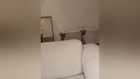 Media: Video of a minimalist living room with beige walls, a large mirror, and three beige armchairs arranged in a semi-circle. The room's design is modern and cozy, with a soft, neutral color palette.