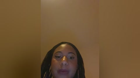 Video of a young African-American woman with medium brown skin, straightened black hair, and subtle makeup. She has a neutral expression, and the background is a plain, beige wall.