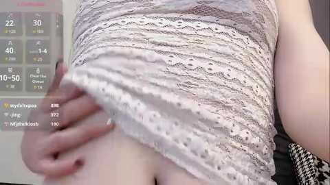 Video of a light-skinned woman in a white lace dress, pulling up the hem to reveal her lower abdomen and pubic area. Background includes a digital display showing weather conditions.