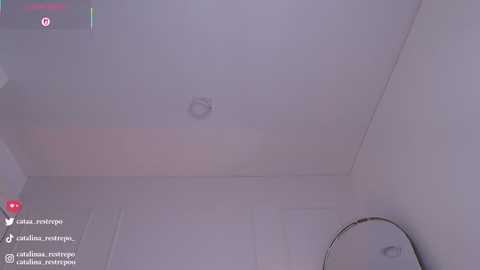 A video showing a dimly lit, white-walled room with a small, circular light fixture in the center. The room appears empty, with a round mirror on the right wall.