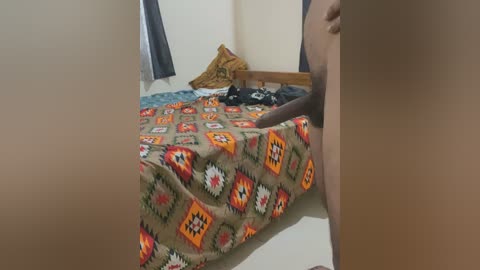 Media: Video of a bedroom with a brown-skinned person's penis visible on a bed with an orange and white patterned blanket, surrounded by pillows.