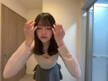 Media: Video of an Asian woman with straight black hair, adjusting her bangs in a modern, minimalist hallway with beige walls and a wooden door. She wears a beige sweater and gray skirt.