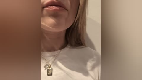 A close-up video of a woman with fair skin, wearing a white t-shirt, and a silver necklace with a rectangular pendant. The image is slightly blurred, focusing on her mouth and neck.