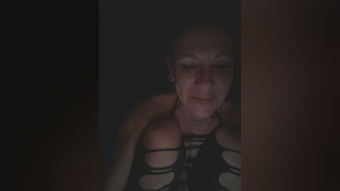 Video of a woman with fair skin, dark hair, and a black, cut-out top, her eyes closed, leaning against a dark background, creating a moody, intimate atmosphere.