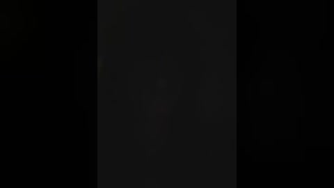 A dimly lit video shows a vertical, dark rectangle against a black background, possibly a doorway or a shadowy figure, creating a mysterious and eerie atmosphere.