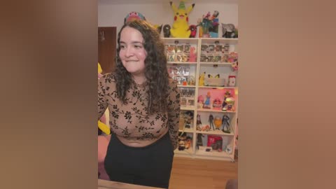 Media: Video of a plus-sized woman with curly hair in a floral top, standing in a Pikachu-themed room with shelves filled with Pok\u00e9mon toys and figurines.