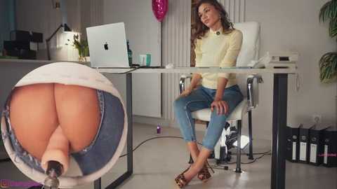 Video of a woman in a modern office with an Apple laptop, jeans, and high heels, sitting on a white chair, wearing a yellow sweater, with a close-up of her bare buttocks in a glass bowl.