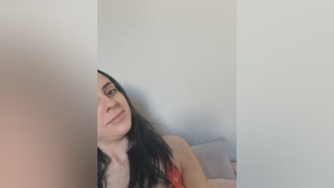 Media: A video of a young woman with long black hair, fair skin, and red lingerie, smiling slightly, leaning against a white wall. The image is cropped and slightly blurry.