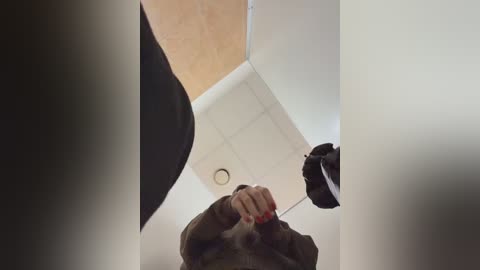 Media: Video of a woman in a dark coat adjusting a black umbrella inside a modern, white ceiling-tiled room. The angle is from the floor looking up, capturing her hands and the umbrella.