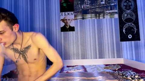 Video of a shirtless young man with a tattoo on his chest, in a dimly lit room with posters and a bed.