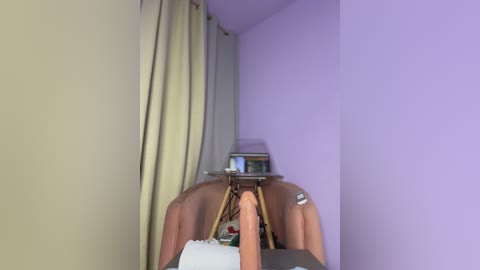 Video of a corner in a room with light purple walls, featuring beige curtains, a small wooden table with a laptop, and a pair of pink Eames chairs.