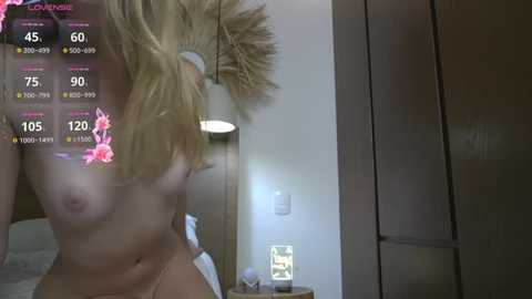 A video shows a naked blonde woman with medium-sized breasts, wearing a white headband, in a dimly lit bedroom with a digital overlay displaying fitness stats.