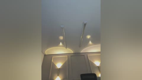Video of a modern, minimalist ceiling with three linear fluorescent lights and two recessed spotlights, creating a soft, ambient glow against a smooth, off-white wall.