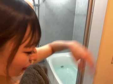 Media: Video of an Asian woman with dark hair in a bathroom, wiping condensation off a glass shower door. She wears a dark top. Background features a white bathtub and stainless steel fixtures.