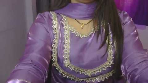 Video of a person wearing a luxurious, shiny purple dupatta with intricate gold embroidery and pearls. The background features purple and white hues.