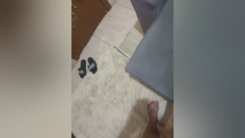 A video of a person's feet, wearing black socks with white writing, standing on a beige carpet. A light blue towel is draped over the person's legs.