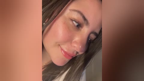 Video of a close-up of a young Caucasian woman with fair skin, straight brown hair, and light makeup, smiling softly, with blurred, tanned male hands framing her face.