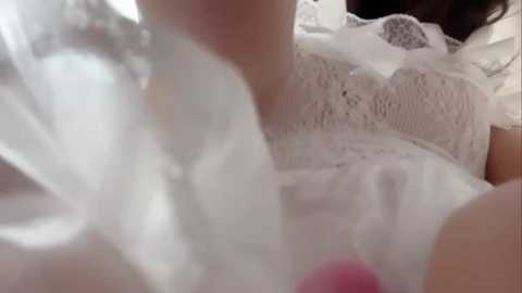 A close-up video of a woman's neck and chest in a white lace top, blurred background, and soft lighting.