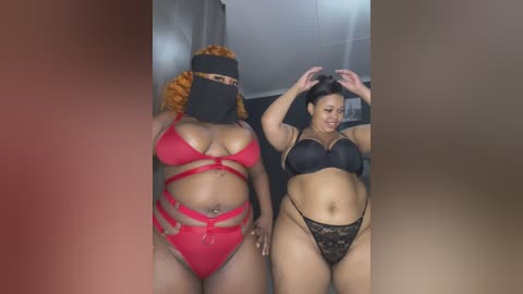 Video of two plus-sized Black women with light skin tones in matching red and black lingerie, adjusting their hair in a dimly lit room.