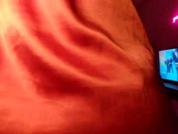 A close-up video of a reddish-brown, textured human skin, possibly a thigh, with a blurry TV screen showing two silhouetted figures in the background.