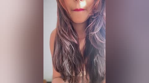 Video of a woman with long, wavy, dark brown hair and red lipstick, partially visible face, wearing a strapless top, against a blurred background.