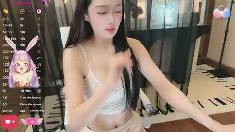 A video of an East Asian woman with long black hair, wearing a white bra, sitting at a piano. The background includes a black curtain and a colorful painting.