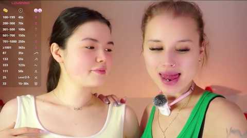 Video of two young women, one with light skin and dark hair, the other with light skin and blonde hair, both smiling, in casual attire, against a pink background.