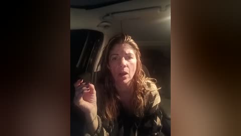 Video of a distressed woman with long, wavy brown hair, wearing a dark jacket, looking out of a car window, with a blurred background.