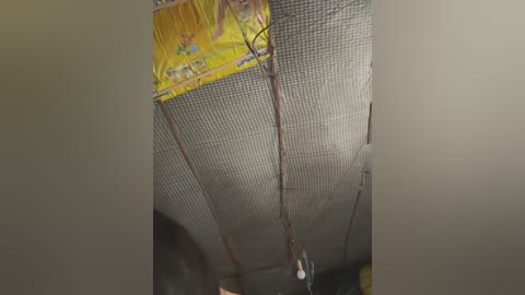 A video showing a close-up view of a ceiling with a yellow, patterned fabric hanging above a mesh screen, with a light fixture dangling below.