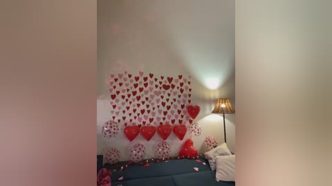 A video of a dimly lit bedroom decorated with red heart-shaped confetti on the wall, a heart-shaped pillow, and a red heart-shaped lampshade on a bedside table.