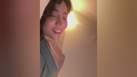 A close-up video of a young Asian woman with short, dark hair, smiling warmly, partially obscured by a beige wall.