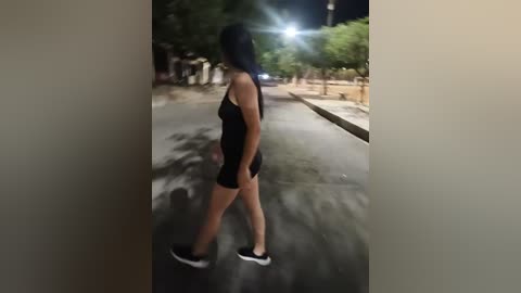 A video of a woman walking on a dark, deserted street at night, wearing a black tank top and shorts, with a streetlight casting a bright glare.