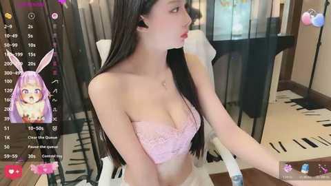 Video of an Asian woman with long black hair and bunny ears, wearing a pink lace bra, sitting at a desk in a modern room with a blackboard.