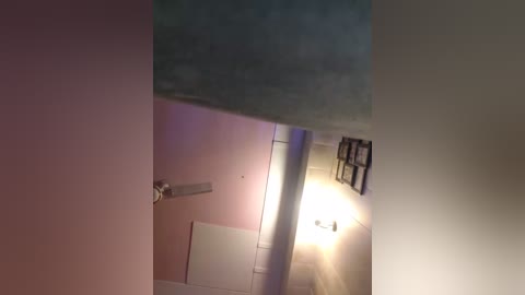 Video of a narrow hallway with light pink walls, a partly open white door, and a dimly lit lamp on the right wall.