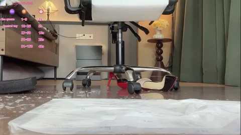 Video of a spilled drink on a modern office chair with a white seat and black base, surrounded by a beige carpet, a green curtain, and a wooden side table with a lamp.