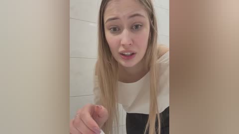 Video of a young, light-skinned woman with long blonde hair, wearing a white and black striped top, peering through a bathroom door, looking surprised.